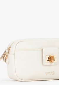 Borsa cosmetica in pelle bianca con hardware dorato, chiusura con zip e patta frontale. Presenta il logo del marchio impresso di lato.