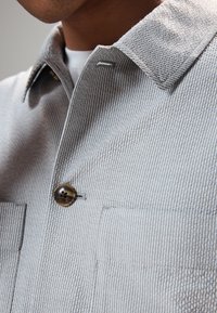 Gray striped shirt with a button closure, featuring a textured fabric, spread collar, and two front pockets on the chest.