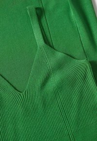 Débardeur vert en tissu côtelé, doté d'un décolleté en V et de fines bretelles. La texture est lisse avec un léger éclat.