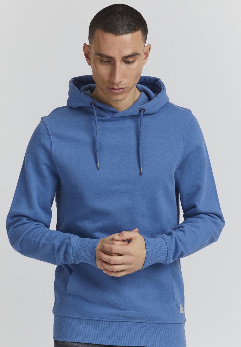 Sudadera de algodón azul con cordón ajustable, bolsillo canguro y puños acanalados. Textura suave y diseño ajustado, con una pequeña etiqueta de marca en el lateral.