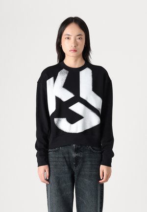 Sudadera negra con un gran gráfico abstracto blanco. Tiene mangas largas y un cuello redondo. Textura suave, corte relajado.