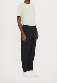 Světle zelené tričko s vyraženým logem "EA7", kombinované s černými cargo kalhotami se bočními kapsami a elastickým pasem, nošeno s bílými teniskami.