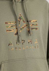 Felpa verde oliva con tasca a marsupio frontale, caratterizzata da un logo e testo con motivo camouflage in colori a contrasto, realizzata in tessuto morbido.