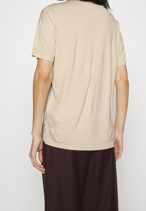 Beige katoenen T-shirt met korte mouwen, losse pasvorm en zijsplitsingen. De stof lijkt glad en licht van gewicht.