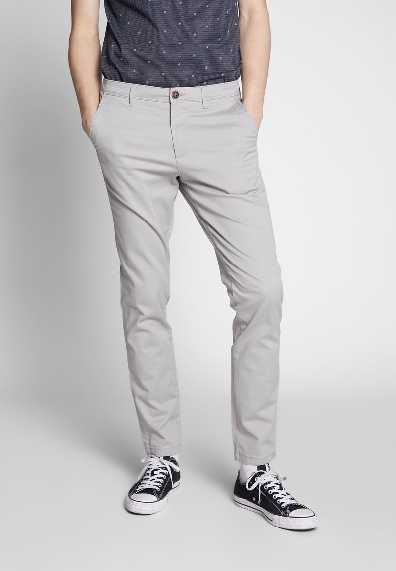 Grå chinos med en slim-fit-design, med knappstängning och sidofickor, i kombination med svarta sneakers och vita snören.