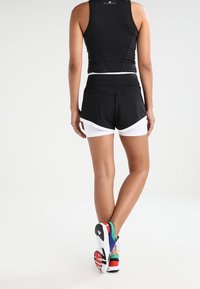 Black athletic tank top and black shorts with white accents, paired with multi-colored running shoes. Focus on sleek design and fit.
