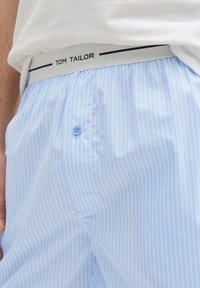 Lichtblauwe herenbroek met witte strepen, voorzien van een grijze tailleband met het label "TOM TAILOR" en een klein blauw knopdetail.