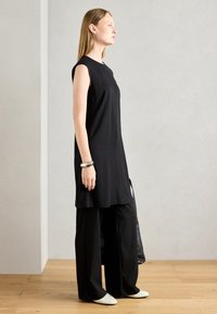 Černé bezramínkové šaty se rovnými liniemi, kombinované s širokými černými kalhotami a bílými balerínami. Jednoduchý design bez viditelných vzorů.