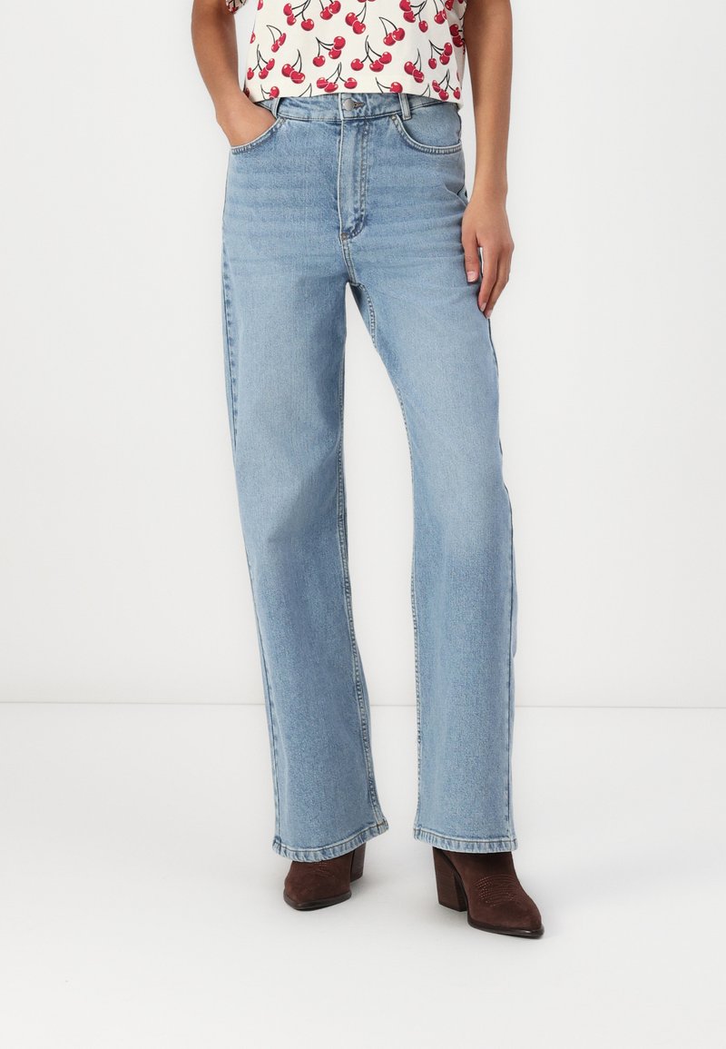 Jeans drepti de culoare albastru deschis, din denim, cu buzunare frontale, talie înaltă și margini tivite. Purtați cu botine maronii cu toc.