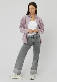 Chemise en velours côtelé violet clair avec fermeture à boutons sur un débardeur blanc, accompagnée d'un jean ample taille haute en denim délavé gris et de baskets blanches.