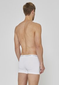 Boxer blanc en coton avec une large ceinture élastique, arborant un logo. Le design est ajusté et sans couture pour un aspect lisse.