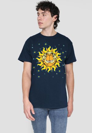 Young man wearing a navy t-shirt with a graphic of a smiling orange cat face inside a yellow sun surrounded by blue stars.