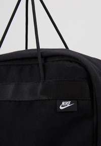 Svart Nike-väska med dragsnörningsstängning, tygtextur och påsydd logotag på frampanelen.