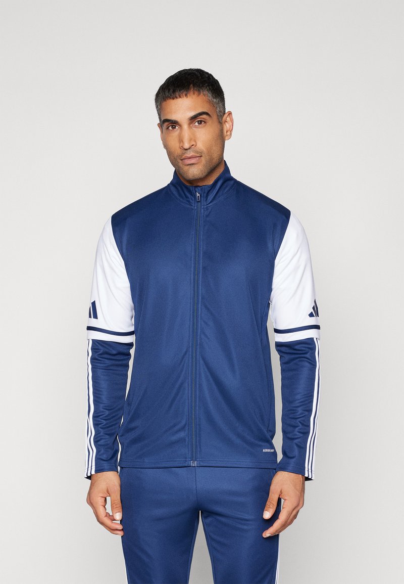 Marineblauw en witte sportjas met een hoge kraag, volledige rits, gladde stof, voorzien van drie strepen op de mouwen en een logo op de borst.