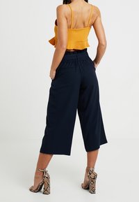 Culottes de color marino con cintura elástica, con un corte relajado y largo hasta el tobillo. Combinados con un top corto de volantes en mostaza y tacones de piel de serpiente.