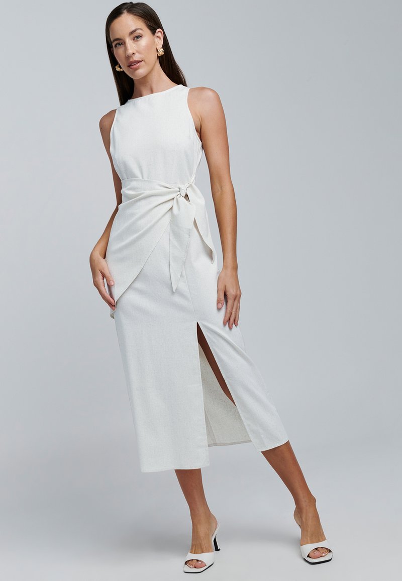 Witte linnenmix jurk met een nauwsluitend lijfje, een gestrikte taille en een zijsplit. Gecombineerd met witte open-toe hakken. Soepele textuur.