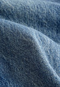 Gros plan sur un tissu en denim bleu avec un motif de tissage diagonal visible et des plis doux.