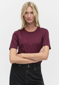 Burgundy puuvillainen t-paita lyhyillä hihoilla ja pyöreällä kaula-aukolla, yhdistetty mustiin farkkupukuihin, joissa on pilkullisia yksityiskohtia.