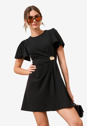 Schwarzes Kleid mit kurzen Puffärmeln, das ein gedrehtes Frontdesign und einen goldenen Knopfakzent an der Taille aufweist. Glatter Stoff, knielang.