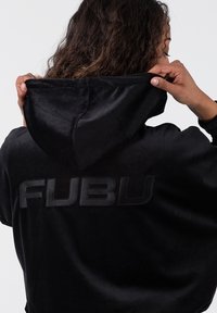 Juodas aksominis džemperis su didžiuliu, subtiliai įspaustu "FUBU" logotipu nugaros dalyje, su šviesos pavidalo kapišonu ir laisvu siluetu.