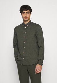 Dunkelgrüne Hemdbluse aus strukturiertem Stoff. Mit weitem Kragen und hellen Holzknöpfen, langen Ärmeln und abgerundetem Saum.