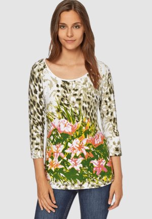 Mujer vistiendo una blusa de manga tres cuartos con estampado de leopardo en las mangas y la parte superior, y un diseño floral rosa en la parte baja frontal.