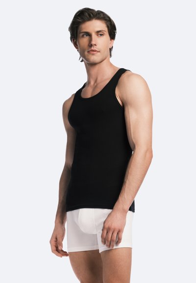 Débardeur noir côtelé sur un modèle, associé à un short de boxeur blanc. Design simple, tissu doux et coupe ajustée.