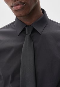 Camisa negra de vestir con cuello puntiagudo y una corbata negra texturizada. Tela suave con un diseño ajustado y detalles de costura visibles.