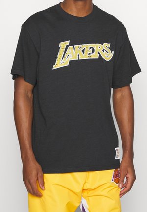 Person trägt ein schwarzes T-Shirt mit abgenutztem gelbem "Lakers"-Text und leuchtend gelbe Basketballshorts mit Lakers-Logo.