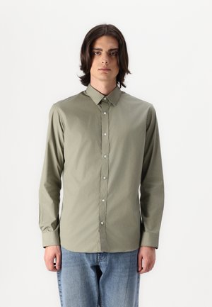 Chemise à manches longues à boutons dans un vert olive atténué, en tissu lisse, dotée d'un col classique et de boutons de couleur claire, associée à un jean bleu.