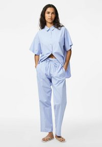 Plava i bijela prugasta kratki rukav košulja s dugmadi uparen s hlačama na vezanje; lagana tkanina, ležeran kroj i ravne sandale.