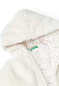 Sudadera con capucha de piel sintética blanca con una textura suave, que presenta un forro interior de lunares en rosa claro y una etiqueta de marca verde en el interior.