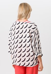 Blouse avec un motif en vagues noir et blanc, coupe ample, manches trois-quarts, poignets volants et accent rose au col.