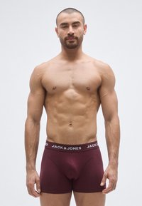 Vīnsarkanas boksa biksītes ar melnu elastīgu jostu un baltu zīmola logotipu. Pieguļošs dizains, izgatavots no mīksta auduma ar gludu tekstūru.