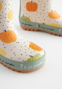 Bottes de pluie à motifs de citrouille jaunes et orange avec un fond crème et des accents verts, dotées d'une semelle en caoutchouc orange texturée.