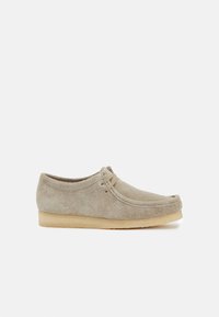 Scarpe in suede di colore beige chiaro con un design basso e arrotondato, dotate di lacci e una suola in gomma beige a contrasto. Texture morbida e dettagli di cucitura minimi.
