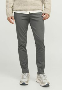 Pantalones gris ajustados hechos de una tela suave, con una textura suave y un diseño minimalista, combinados con zapatillas deportivas gris claro.