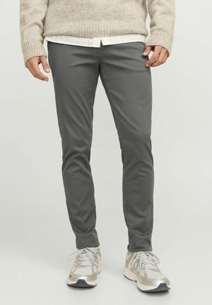 Šedé slim-fit kalhoty vyrobené z měkké tkaniny, s hladkou texturou a minimálními detaily, spárované se světle šedými sportovními botami.