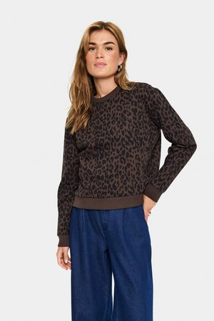 Sweatshirt à imprimé léopard brun avec un col rond et des manches longues. Poignets et ourlet côtelés ; porté avec un pantalon en denim bleu ample.