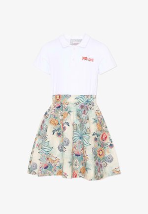 Witte polojurk met het "Just Cavalli"-logo op de borst en een kleurrijke rok met bloemen- en dierenprint.
