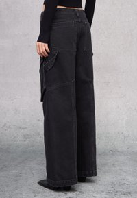 Pantalones cargo anchos negros con diseño de patchwork, múltiples bolsillos y costuras visibles. Hechos de denim con un acabado texturizado.