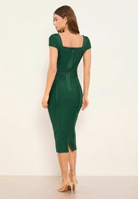 Zöld testhez simuló ruha négyzet alakú nyakkivágással, bordázott textúrával, testhezálló sziluettel, hátul cipzárral és combhasítékkal. Pántos, bézs színű magassarkúval párosítva.
