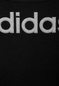 Tessuto nero con grande logo "adidas" argentato e luccicante. Il materiale presenta un motivo a maglia testurizzato con una finitura liscia.