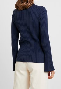 Ribbat marinblå tröja med långa ärmar, med en figursydd silhuett och utsvängda ärmslut. Tillverkad av mjukt, texturerat tyg.
