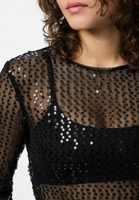 Crna prozirna bluzica s uzorkom od sequina; ima okrugli izrez i duge rukave, stvarajući teksturirani izgled s sjajnim naglascima.
