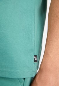 Turkusowa bawełniana koszulka t-shirt z przeszytym dołem i małą czarną metką Nike po bokach. Gładka faktura, krótki rękaw.