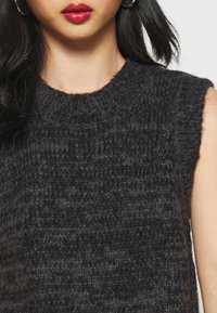 Maglione lavorato a maglia scuro con collo alto e design senza maniche. La texture prominente presenta un motivo a costine, aggiungendo profondità e dimensione.