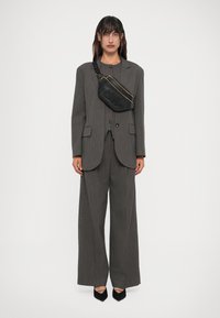 Fato cinza risca de giz com um corte solto, apresentando um blazer com dois botões e calças de perna larga. Uma pequena bolsa preta com detalhes em ouro é usada a tiracolo.