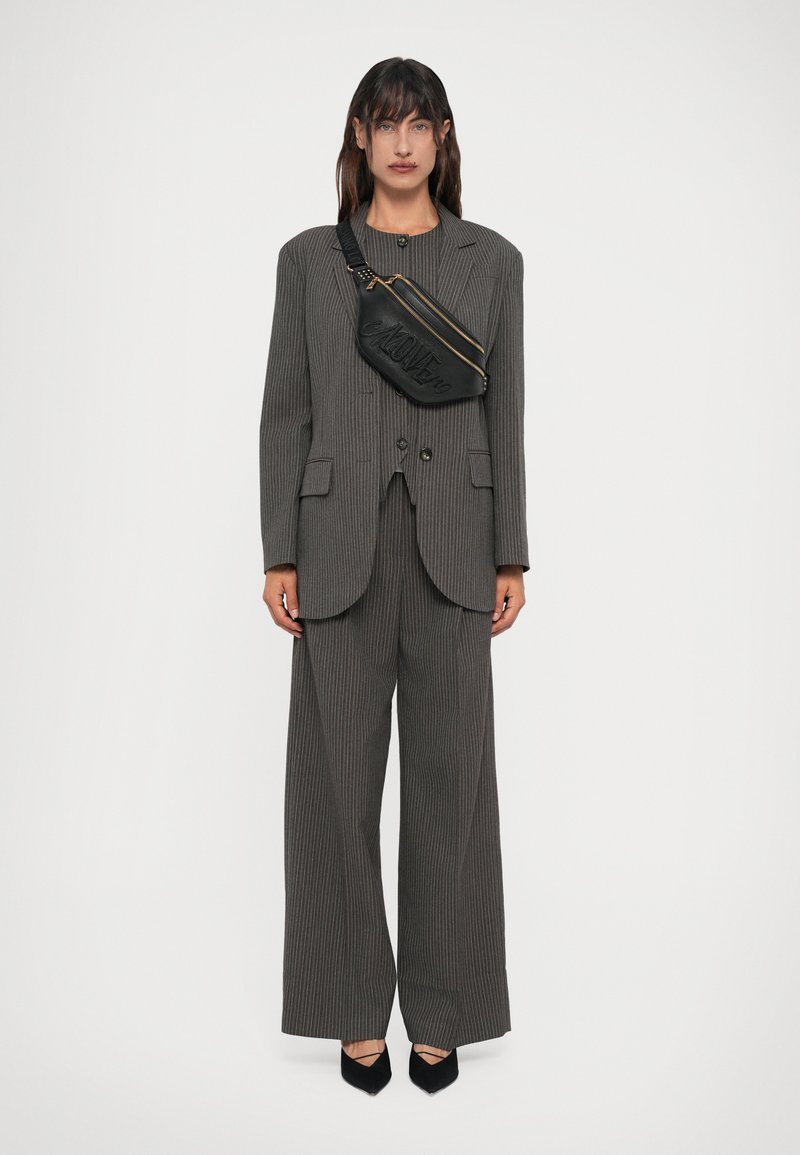 Fato cinza risca de giz com um corte solto, apresentando um blazer com dois botões e calças de perna larga. Uma pequena bolsa preta com detalhes em ouro é usada a tiracolo.