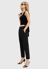 Top corto nero abbinato a pantaloni neri a sigaretta e sandali aperti neri con tacco. L'outfit presenta un design semplice e snellito con tasche.